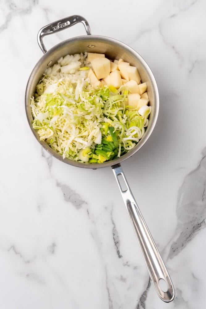 Vegetables included in colcannon soup recipe added to stainless steel soup pot.