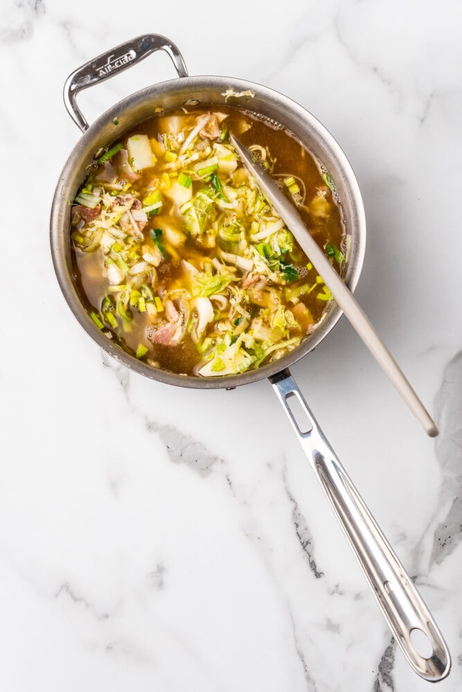 Adding broth to cooked vegetables in colcannnon soup.