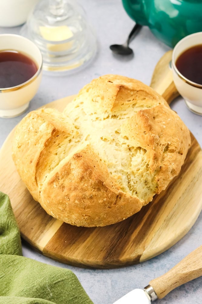 Loaf of authentic Irish soda bread on a wood block with tea and butter on the side.