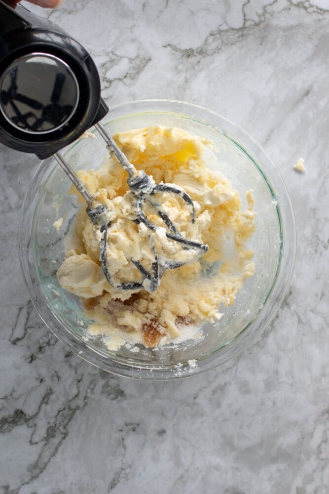 Overhead shot of beating together the butter, cream cheese, vanilla extract, and Splenda in a large glass mixing bowl.