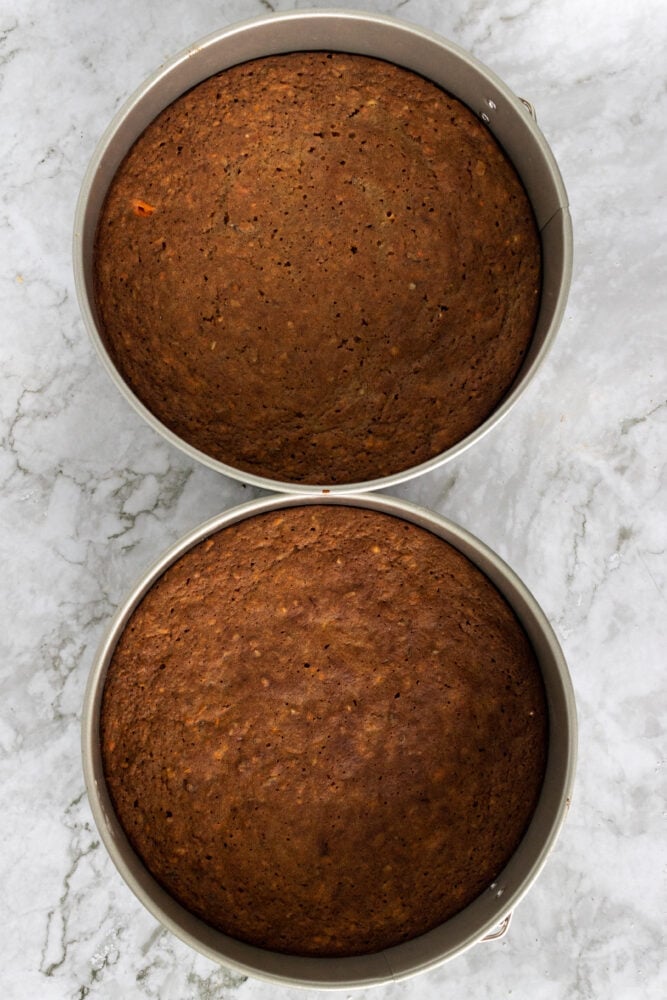 Overhead look into two cake pans with the gluten-free carrot cakes in them baked to a golden brown.