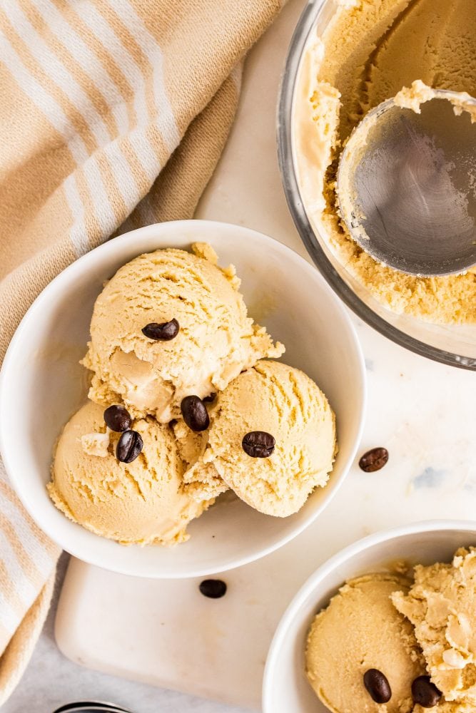 Overhead view of three scoops of coffee gelato in a bowl, topped with coffee beans for garnish.