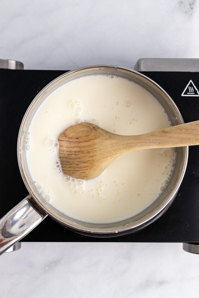 Milk in a saucepan with a wooden spoon.