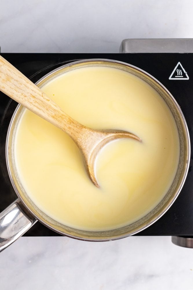 Milk, egg yolks, sugar, and cream in sauce pan with a wooden spoon.