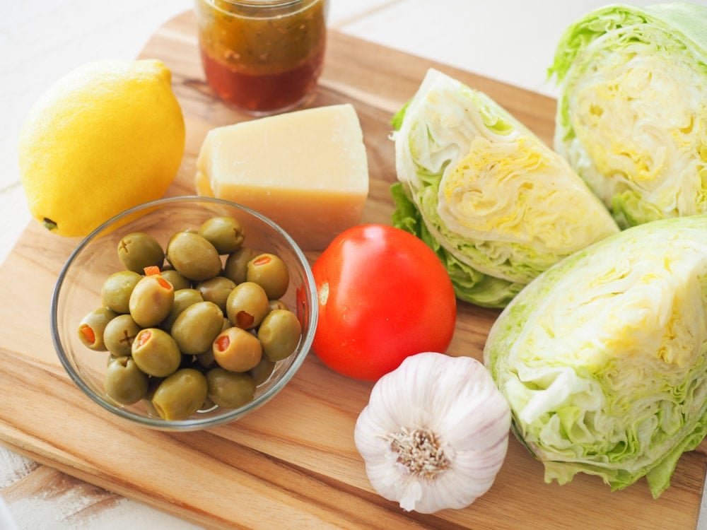 Ingredients for the 1905 Salad on a cutting board: Spanish Olives, Lemon, Parmesan Cheese, Tomato, Garlic, Lettuce.