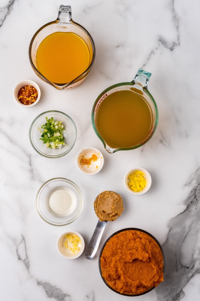 Ingredients for Thai pumpkin soup measured out and displayed on white marble.