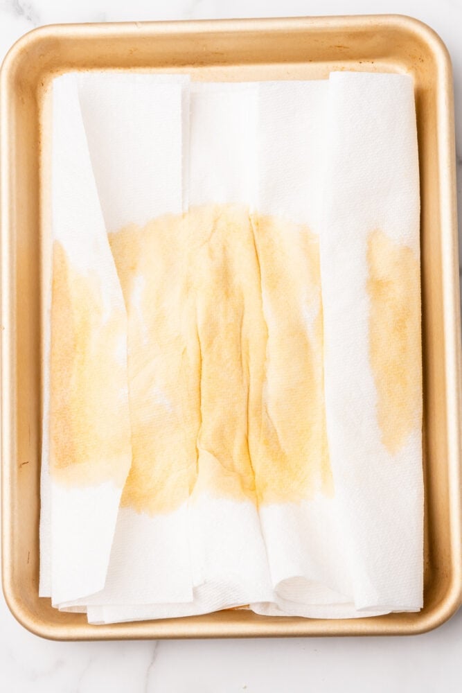 Canned pumpkin getting pressed between white paper towels to remove excess moisture. You can see the moisture pull through on the top of the paper towels.