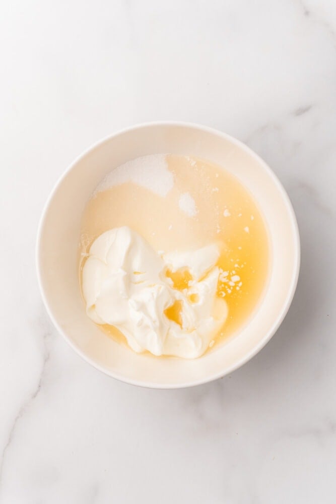 Sour cream, sugar, and bourbon in a white bowl, ready to be mixed into bourbon cream.