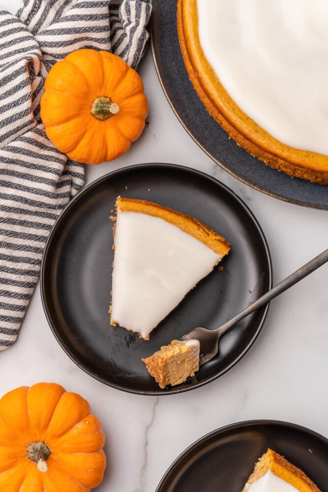 Pumpkin cheesecake slice on top of black plate, there's a bite on a fork next to it, and mini pumpkins surrounding as decoration.