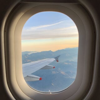 Photo looking out of oval airplane window at tip of the wing of a plane over mountains.