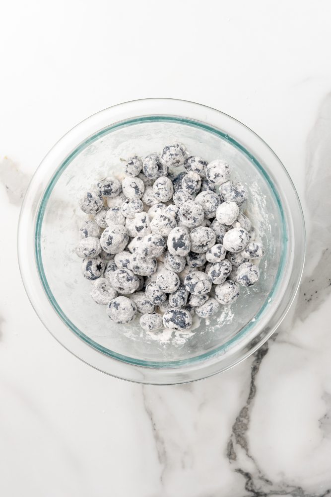 Flour coated frozen blueberries in a clear glass bowl.