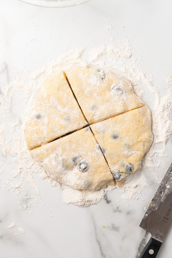 Blueberry scone dough pressed into a flat round shape and cut into four scones.