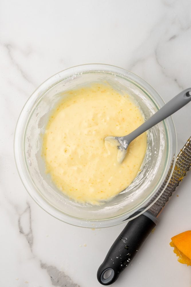  A bowl of orange glaze cake icing. The color is light orange yellow with darker orange specks.