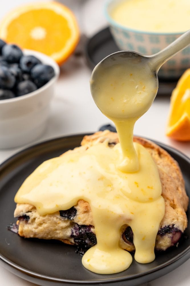 Blueberry scone on a black plate with orange glaze being poured on top.
