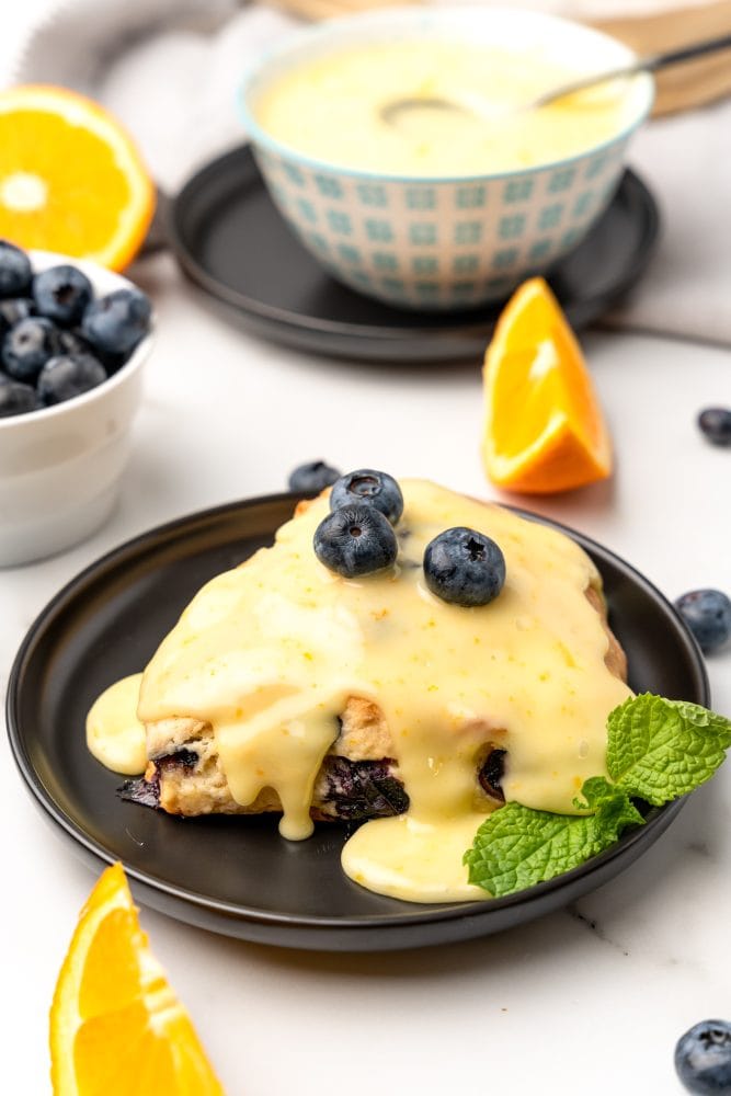 Blueberry scone topped with orange glaze and fresh blueberries, garnished with a side of mint.