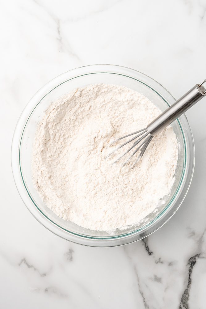 Clear mixing bowl filled with flour and a whisk.