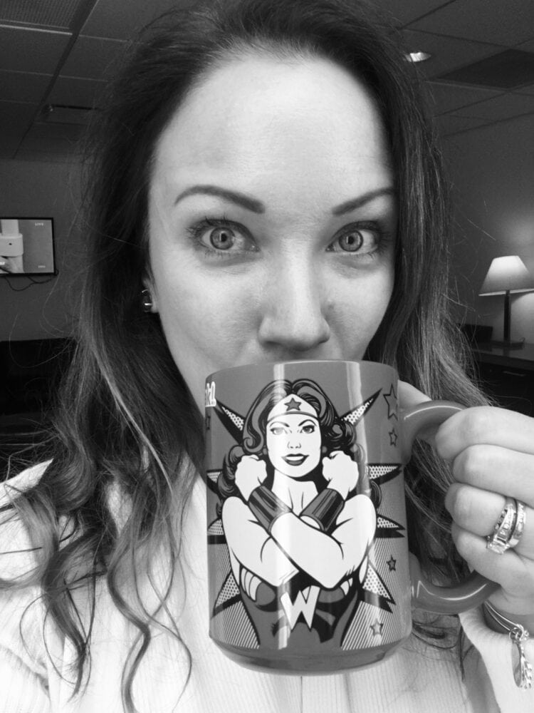 Rachelle sipping coffee out of a Wonder Woman mug.