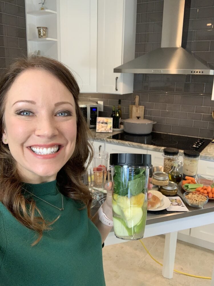 Rachelle holding a green smoothie in her kitchen.