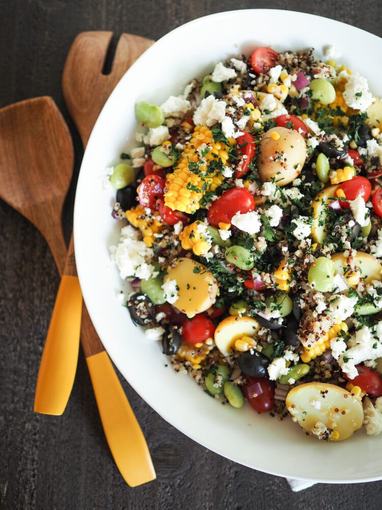 Overhead shot of large bowl of quinoa salad with salad utensils.