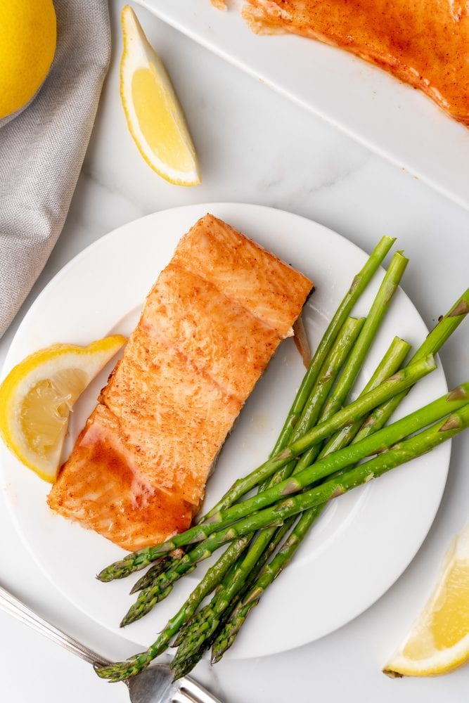 Overhead look of white plate with single serving of sockeye salmon, lemon slices, and asparagus. 