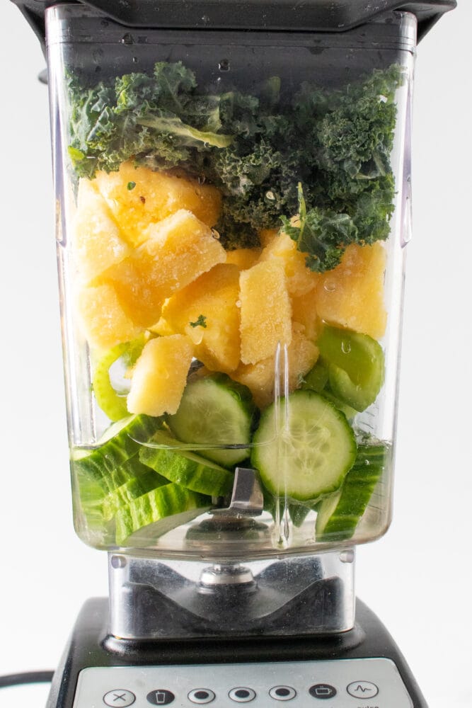 Layered pineapple kale smoothie ingredients in a blender.