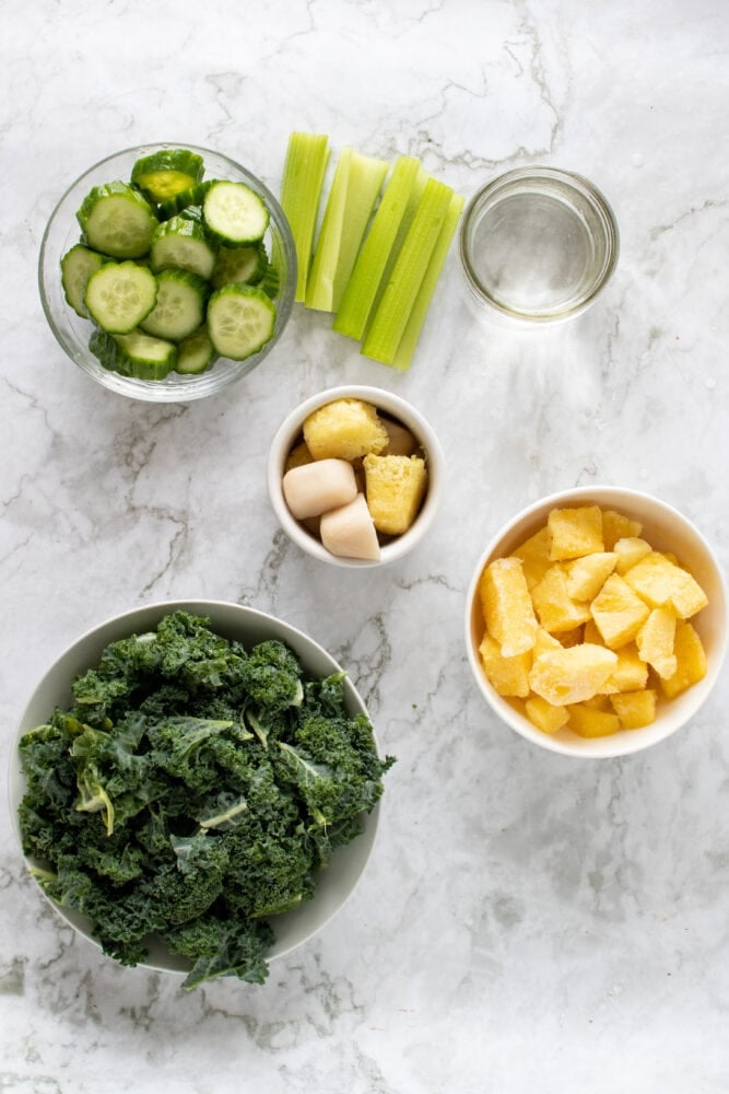 Measuring out the ingredients for the pineapple kale green smoothie including: cucumber, celery, ginger, pineapple, kale, and water.