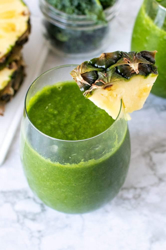 Pineapple Kale Green Smoothie in a stemless wine glass with a wedge of pineapple as garnish.