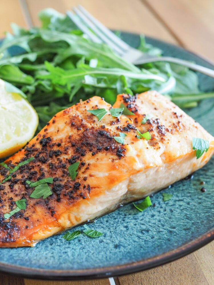 Close up of tajin (chili lime seasoning) on air fried salmon plated on a blue dish with arugula and lemon.