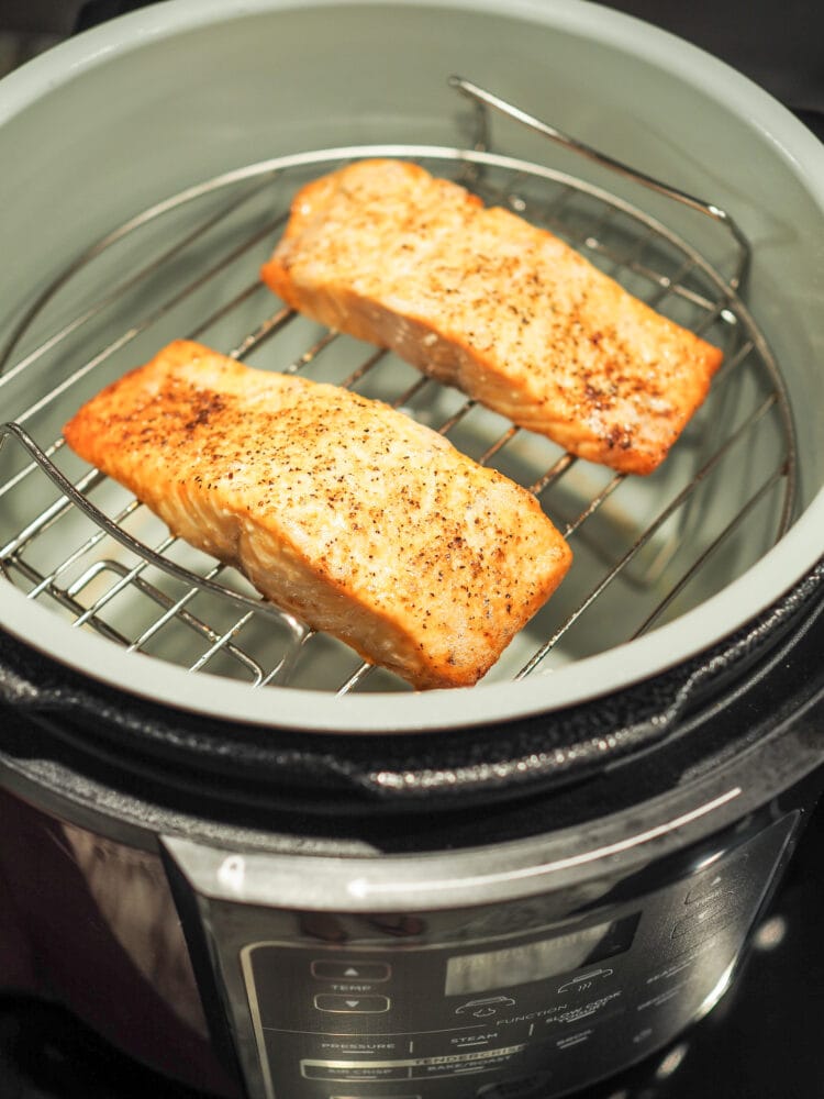 Cooked salmon filets, seasoned with salt and pepper, on a roasting rack inside a Ninja Foodi air fryer.