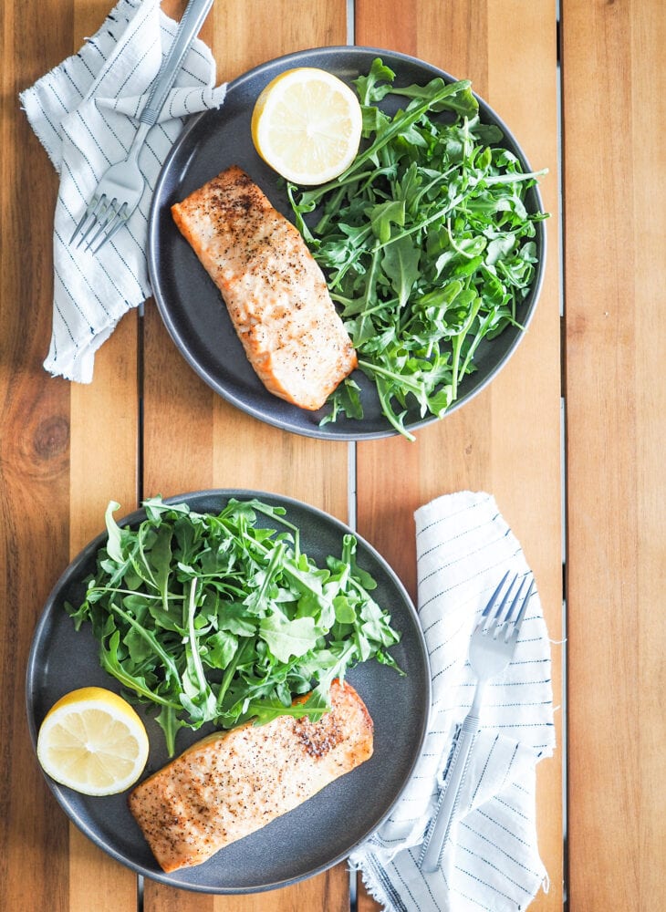 Overhead shot of two gray plates with air fried salmon, arugula, and lemon slices.