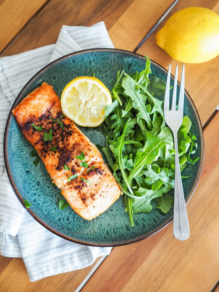 Close up of tajin (chili lime seasoning) on air fried salmon plated on a blue dish with arugula and lemon.