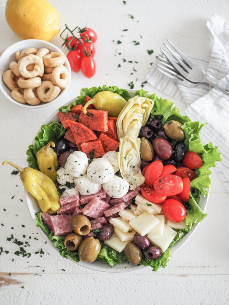 Antipasto Salad with romaine lettuce, salami, soppressata, pepperoncini, olives, mozzarella, provolone cheese, and marinated artichoke hearts. With a side of tarralli crackers and lemon and tomatoes for garnish.