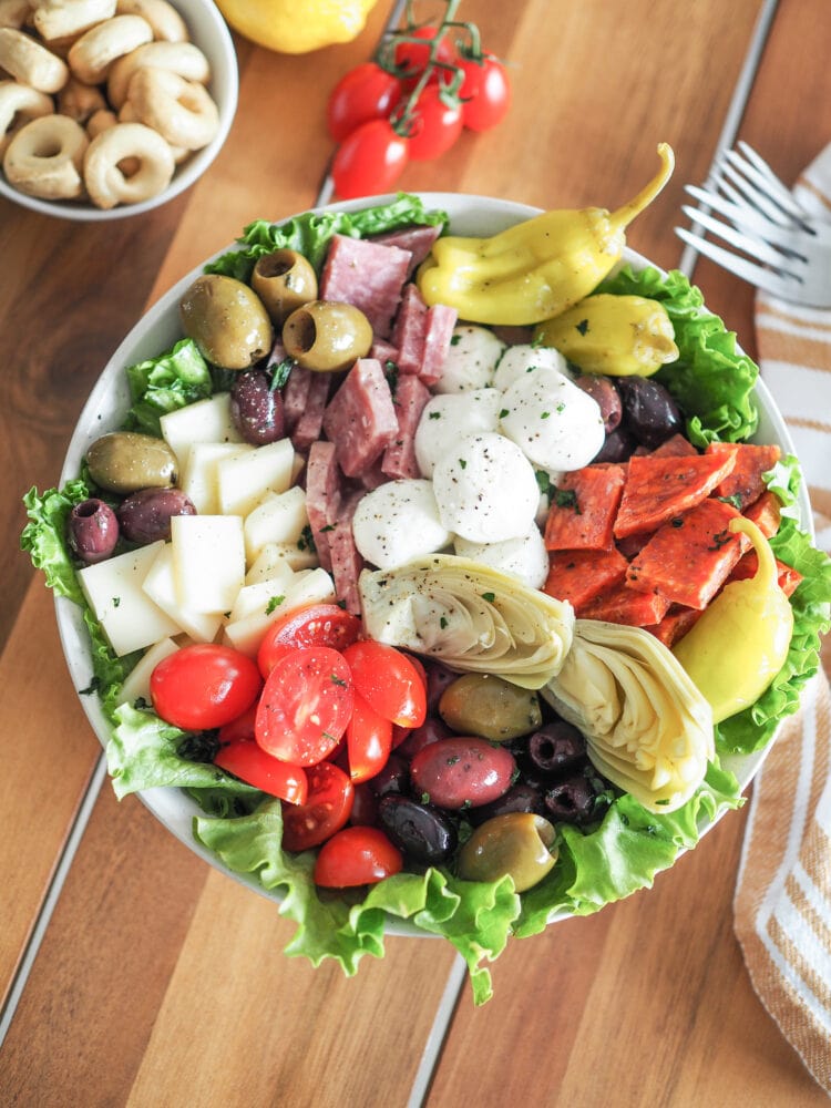 Antipasto Salad with romaine lettuce, salami, soppressata, pepperoncini, olives, mozzarella, provolone cheese, and marinated artichoke hearts. With a side of tarralli crackers and lemon and tomatoes for garnish.