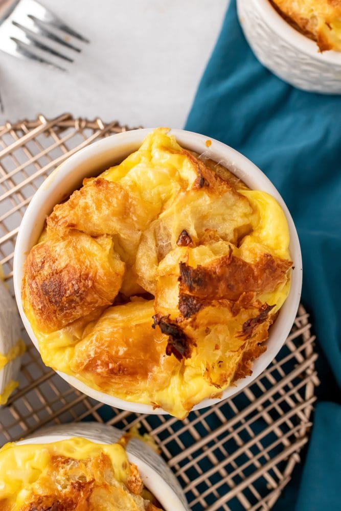 A single ramekin of croissant bread pudding cooling on a wire rack.