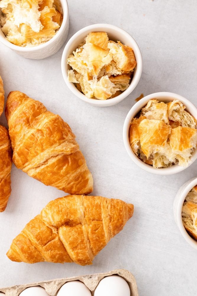 Filling each ramekin with torn pieces of croissants.