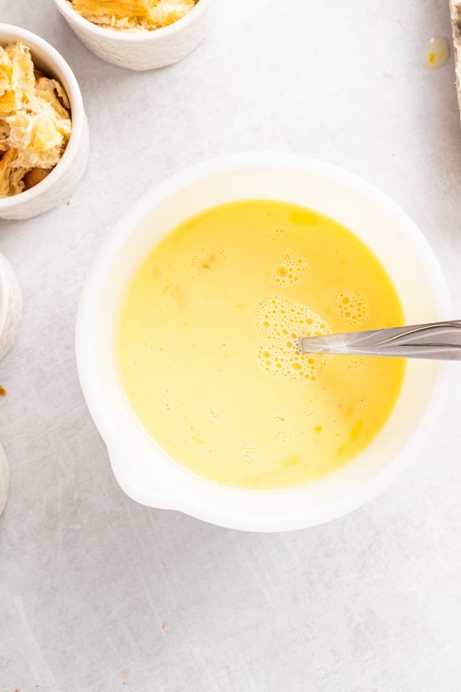 Mixing together eggs, milk, Grand Marnier and sugar in a bowl.