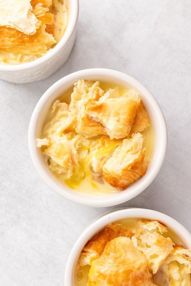 Overhead view of ramekin with torn croissants soaking the egg mixture.