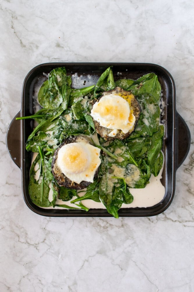 Completed recipe for stuffed mushrooms: Overhead shot of eggs on mushroom caps over a bed of spinach.