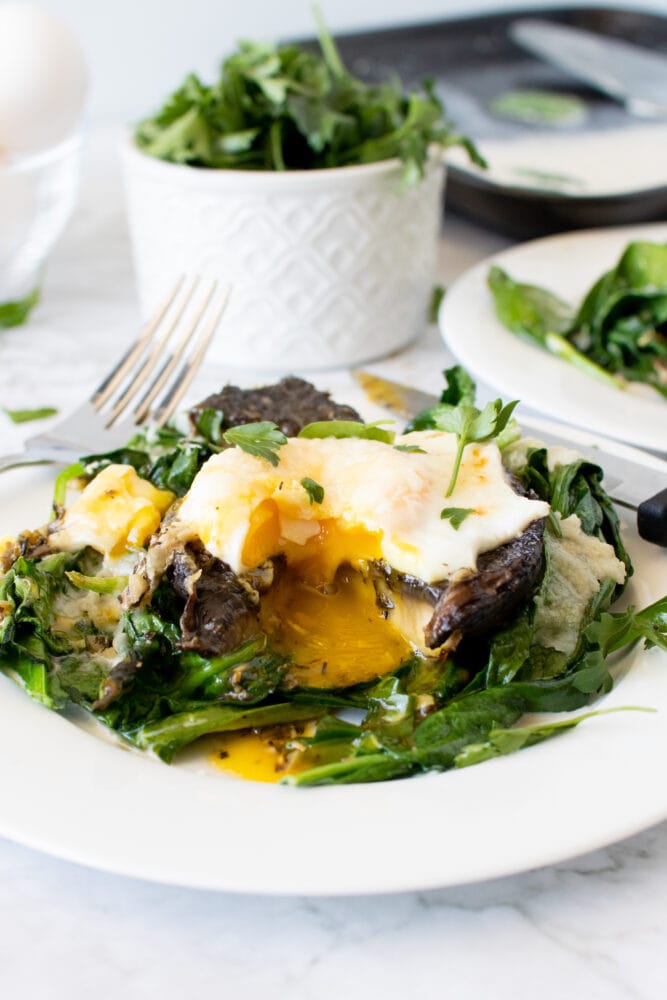 Final shot of baked portobello mushrooms with a bite taken and runny egg yolk mixing with the sauce and spinach.