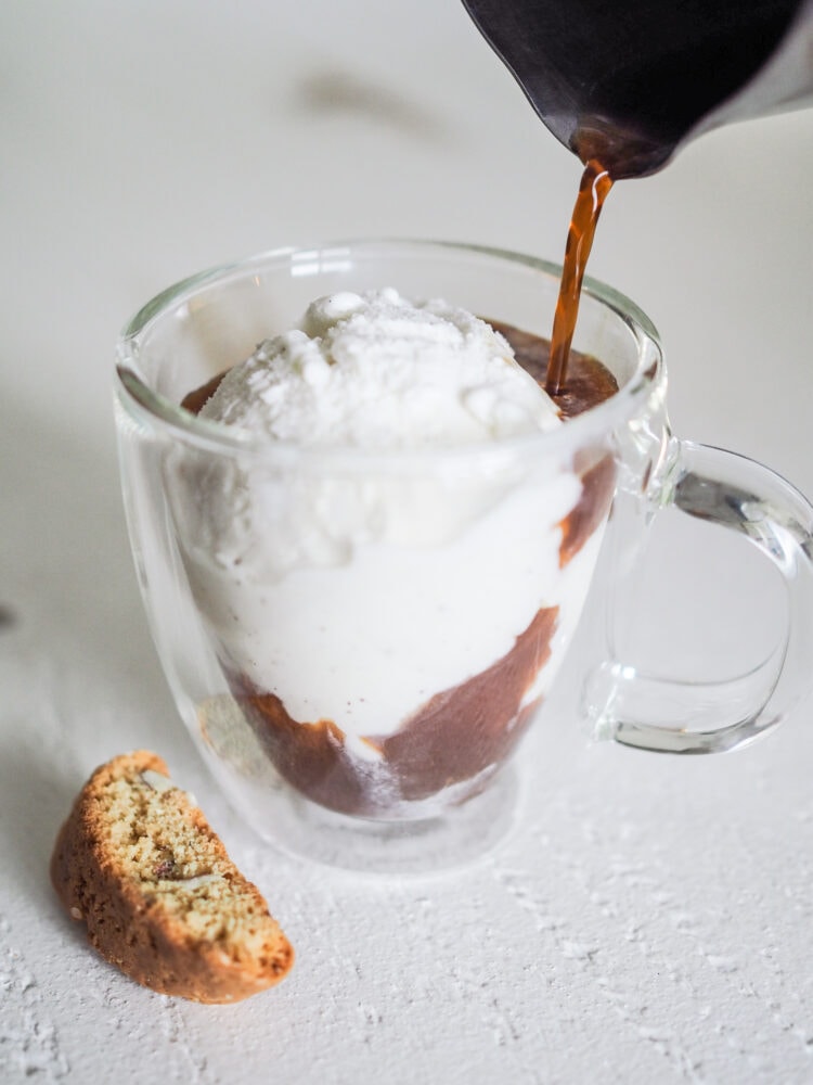 Pouring espresso into a clear glass with vanilla ice cream to make an affogato with a biscotti on the side.