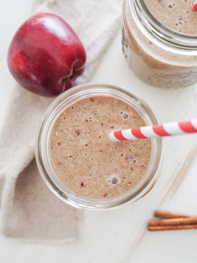 Close up overhead shot of apple smoothie showing red flakes of apple in a delicious looking tan smoothie.