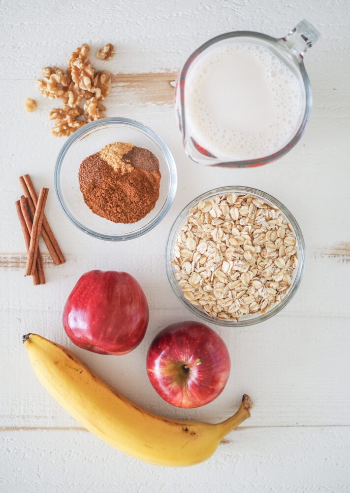 Overhead shot of apple smoothie ingredients including walnuts, oat milk, spices, oatmeal, apples, and banana.