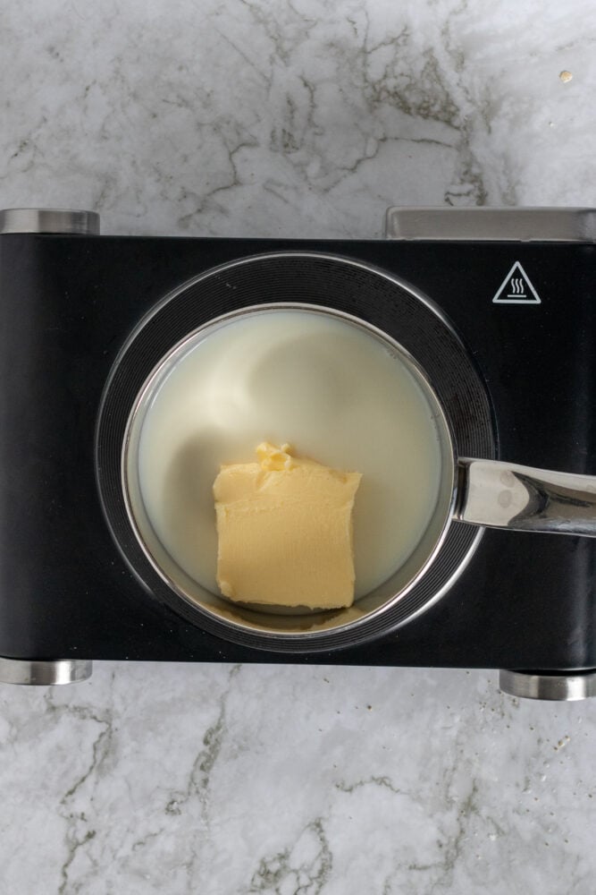 Overhead view of melting butter in a saucepan filled with milk.