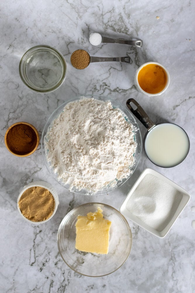 Overhead view of the ingredients needed for this homemade cinnamon roll recipe: sugar, flour, butter, yeast, egg, cinnamon, brown sugar, and milk.
