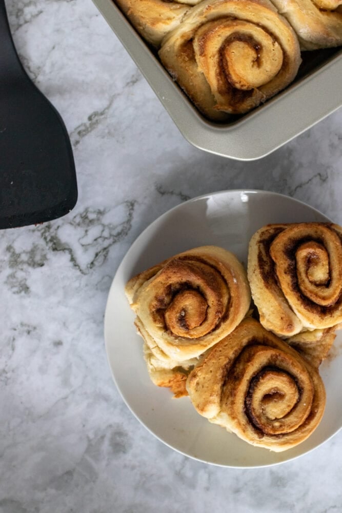 Three homemade cinnamon rolls on a plate with baking pan on the side.