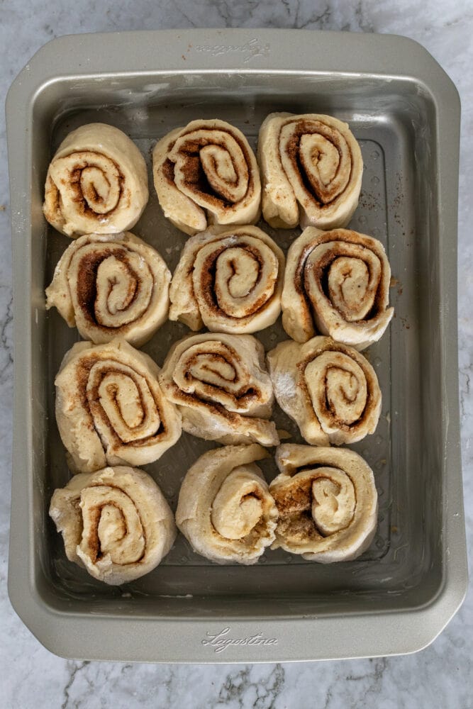 Looking down into metal baking pan with homemade cinnamon rolls laid out ready to be baked.