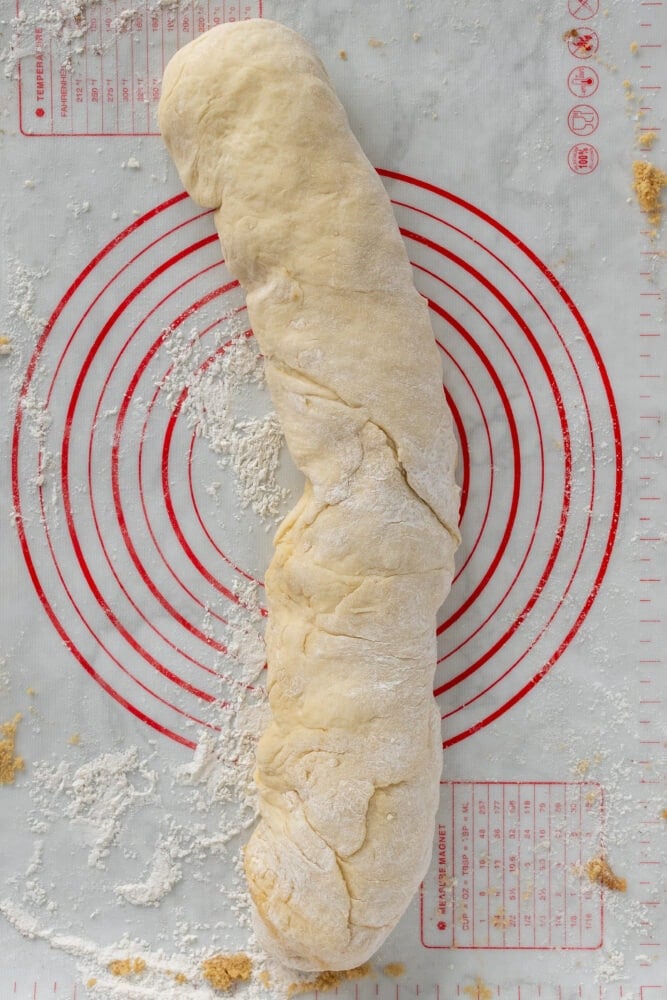 Overhead look at the cinnamon roll dough rolled and pinched together at the ends, resembling a long burrito.