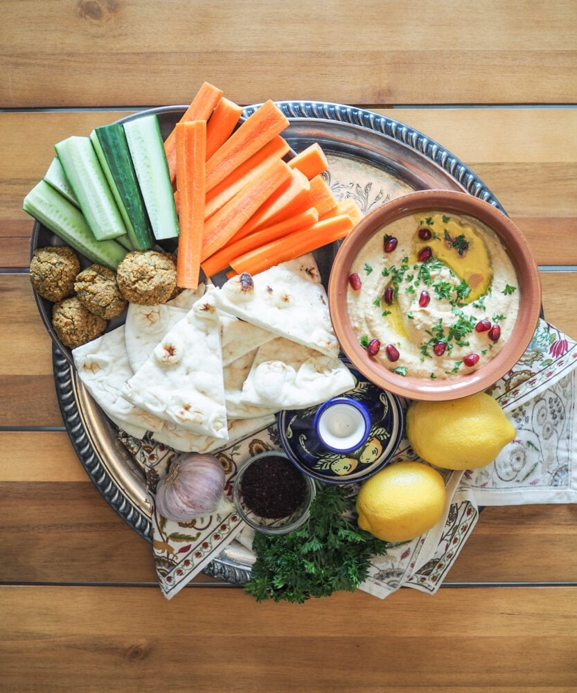 A mezze platter with cucumber, carrots, falafel, naan, and baba ganoush. Also, for decoration, garlic, lemon, parsley, and a blue tagine. 