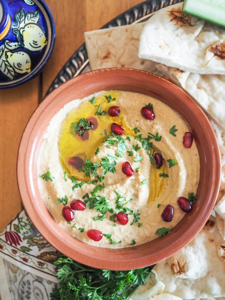 Overhead shot of baba ganoush garnished with parsely, pomegranate, and olive oil. Served with naan.