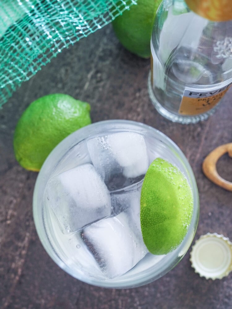 Overhead photo of a single gin and tonic garnished with lime, and limes and tonic bottle in the background.